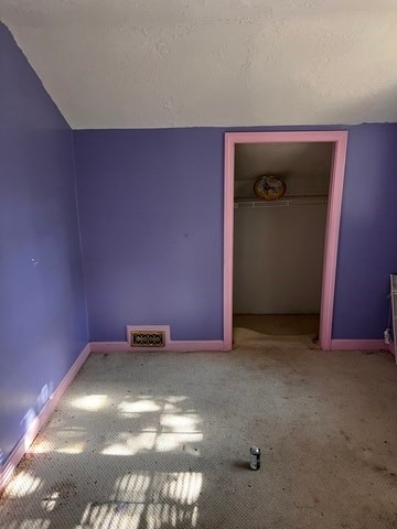 unfurnished bedroom featuring carpet flooring, a textured ceiling, a closet, and lofted ceiling