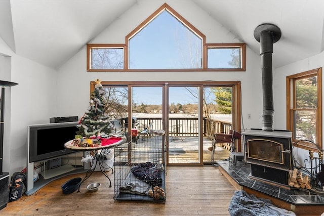 living room featuring wood-type flooring, a wood stove, a wealth of natural light, and high vaulted ceiling