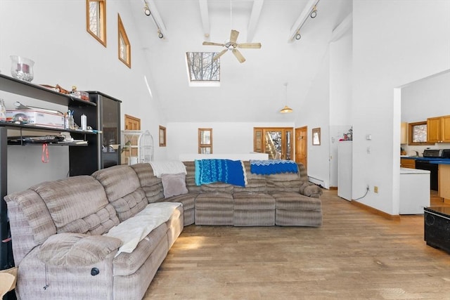 living room featuring rail lighting, a high ceiling, ceiling fan, beam ceiling, and light hardwood / wood-style flooring