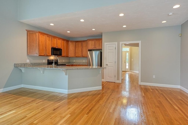 39 Balancing Rock Dr Unit 39, Holliston, MA 01746 - kitchen featuring appliances with stainless steel finishes, a peninsula, a kitchen breakfast bar, brown cabinetry, and light wood-type flooring