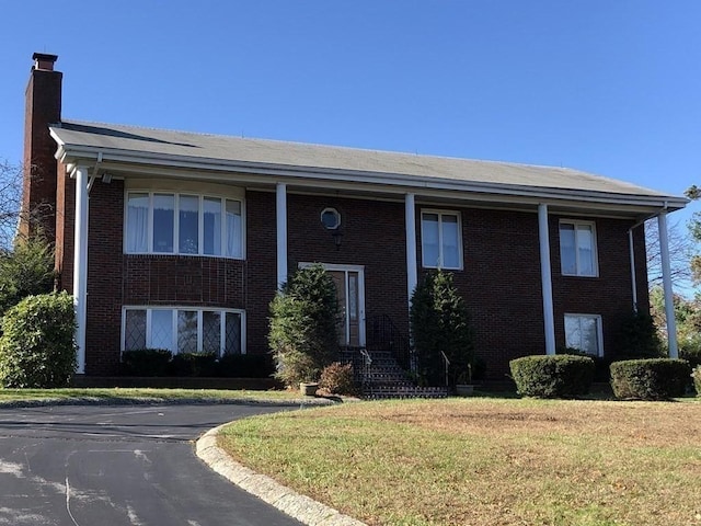 split foyer home with a front yard, a chimney, and brick siding