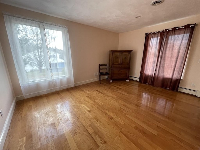 empty room featuring a baseboard heating unit, light wood finished floors, visible vents, and baseboards