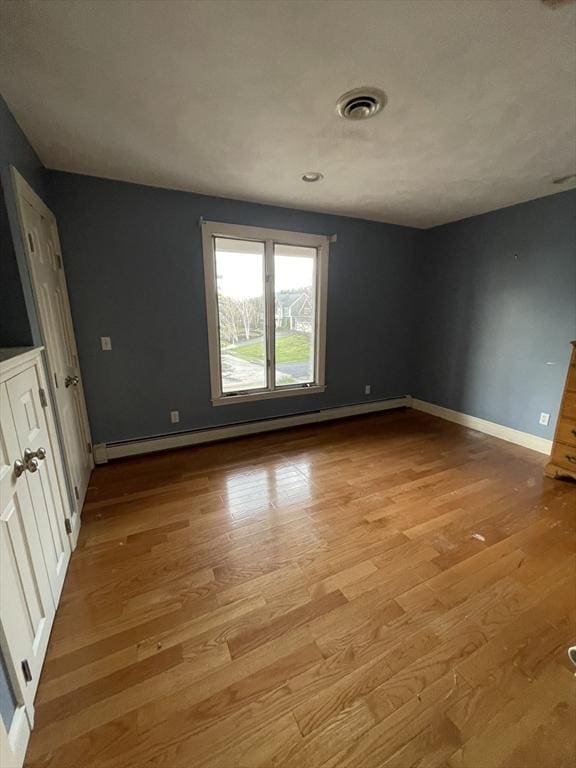 unfurnished bedroom with a baseboard heating unit, light wood-type flooring, visible vents, and baseboards