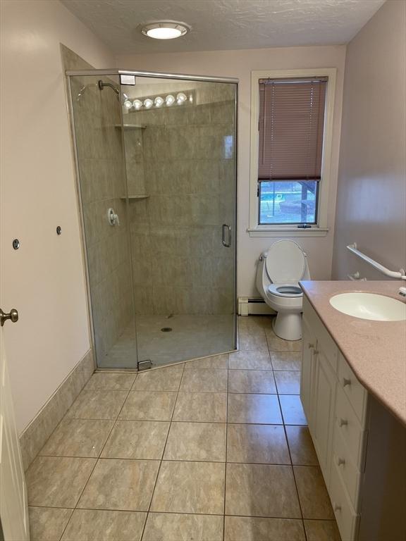 bathroom featuring a textured ceiling, tile patterned flooring, toilet, vanity, and a shower stall