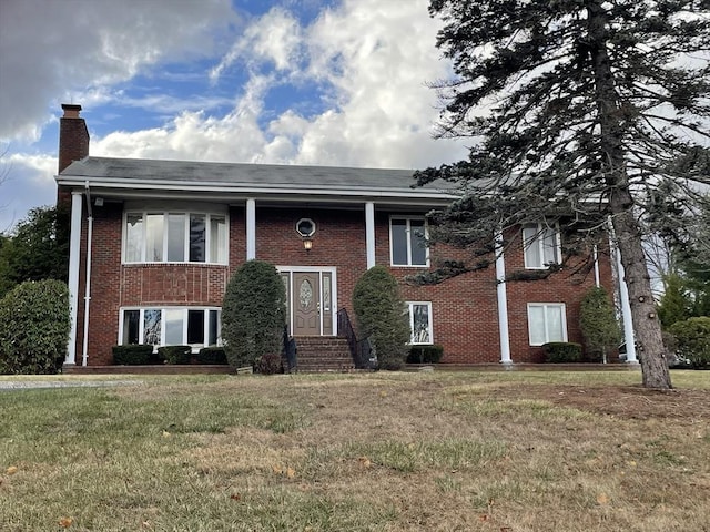 raised ranch featuring brick siding, a front lawn, and a chimney