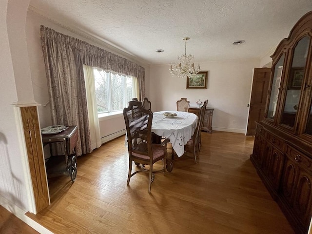 dining room with a textured ceiling, baseboards, baseboard heating, light wood-type flooring, and an inviting chandelier