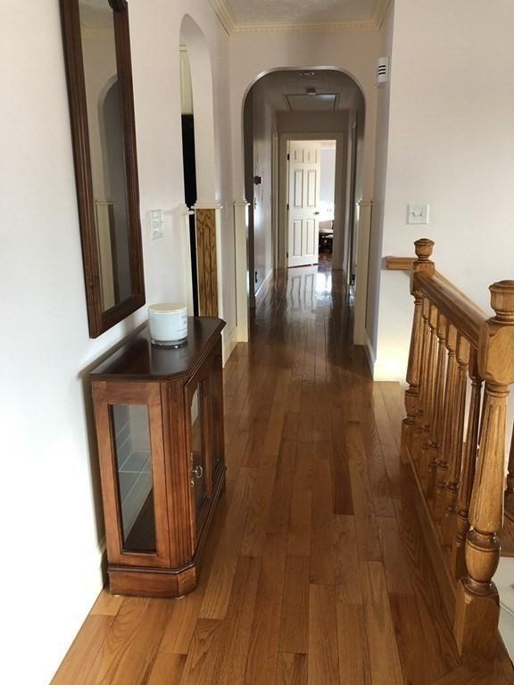 hall featuring arched walkways, dark wood-style flooring, baseboards, and crown molding