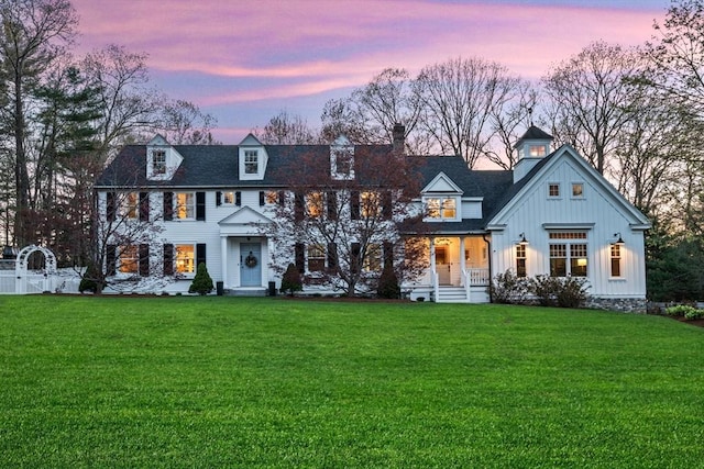 view of front of house featuring board and batten siding, covered porch, a chimney, a gate, and a yard