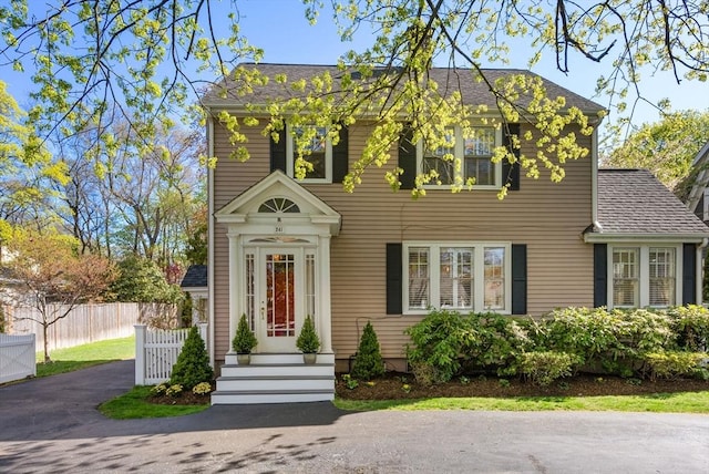 colonial inspired home with a shingled roof and fence