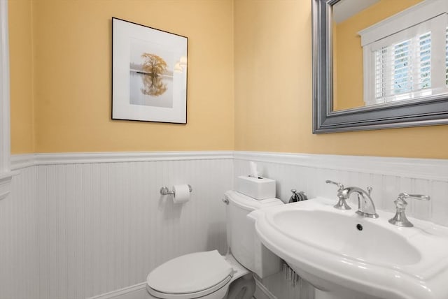 half bathroom with a sink, a wainscoted wall, and toilet