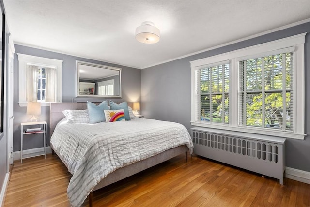 bedroom featuring radiator heating unit, baseboards, crown molding, and wood finished floors