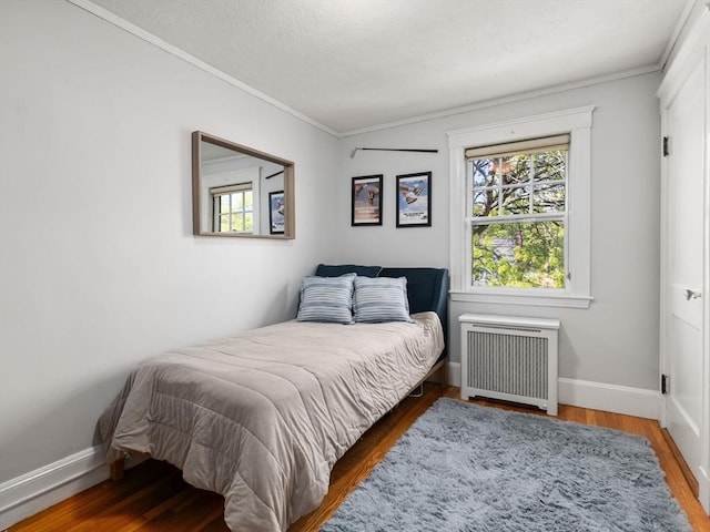 bedroom with ornamental molding, radiator heating unit, and wood finished floors
