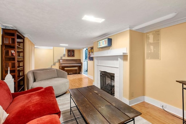 living area with stairs, baseboards, a brick fireplace, and wood finished floors
