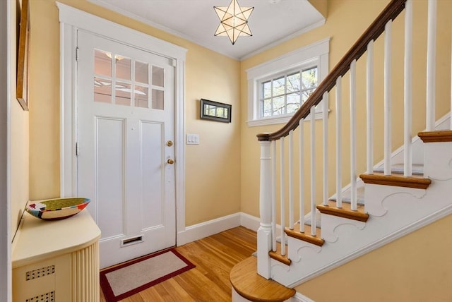 foyer entrance with baseboards, ornamental molding, stairs, and wood finished floors