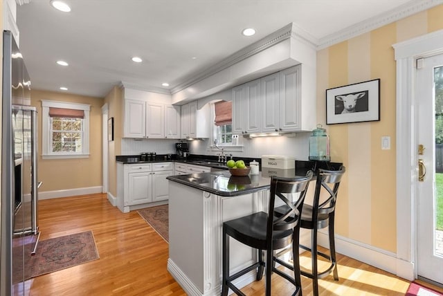 kitchen featuring crown molding, baseboards, light wood finished floors, and a peninsula
