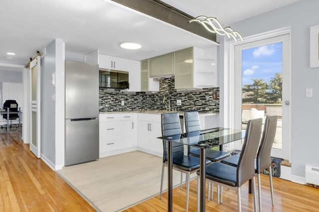 kitchen with stainless steel built in refrigerator, a barn door, light hardwood / wood-style floors, decorative backsplash, and white cabinets