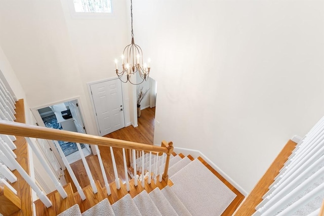 stairs with a chandelier, baseboards, a high ceiling, and wood finished floors