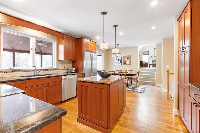 kitchen featuring a kitchen island, pendant lighting, light wood-type flooring, appliances with stainless steel finishes, and a sink