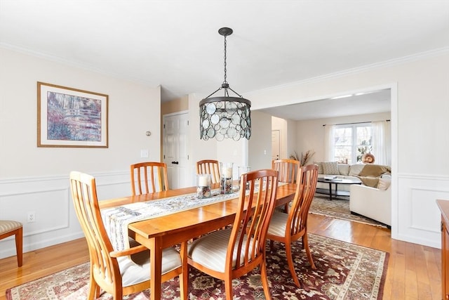 dining area featuring light wood finished floors, a wainscoted wall, a decorative wall, and crown molding