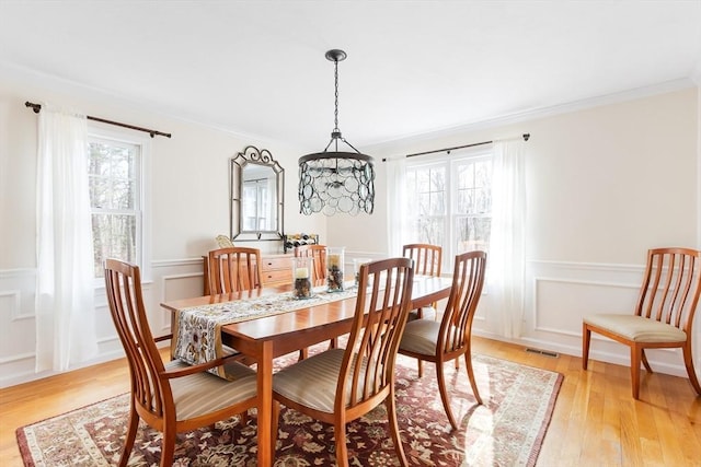 dining space with a wainscoted wall, visible vents, ornamental molding, a decorative wall, and light wood-type flooring