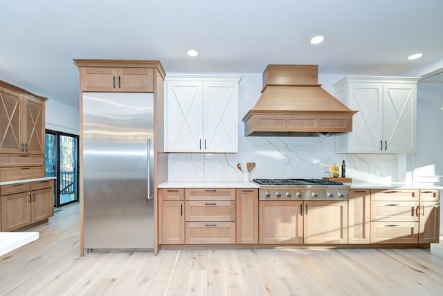 kitchen with light brown cabinets, tasteful backsplash, light hardwood / wood-style flooring, premium range hood, and appliances with stainless steel finishes