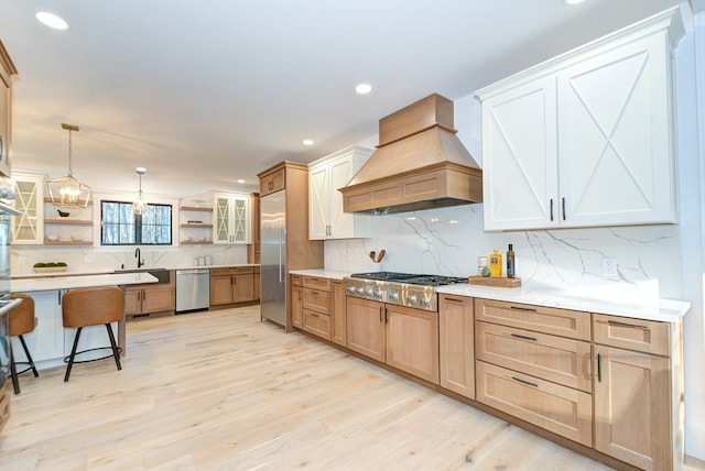 kitchen featuring a kitchen bar, light wood-type flooring, premium range hood, stainless steel appliances, and decorative light fixtures