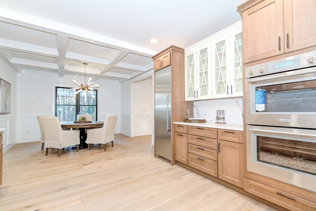 kitchen with coffered ceiling, stainless steel appliances, beam ceiling, light hardwood / wood-style flooring, and a notable chandelier