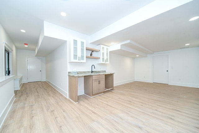 kitchen with white cabinets, light hardwood / wood-style floors, light stone countertops, and sink