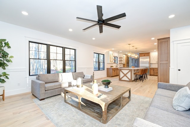 living room with sink, light hardwood / wood-style floors, and ceiling fan with notable chandelier