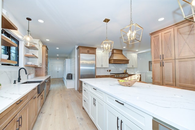 kitchen featuring light wood-type flooring, custom exhaust hood, sink, white cabinetry, and hanging light fixtures