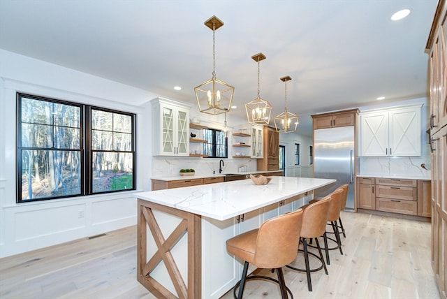 kitchen featuring backsplash, a spacious island, stainless steel built in fridge, light wood-type flooring, and a kitchen bar