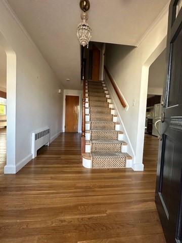 283 Woodland Rd, Newton, MA 02466 - staircase with arched walkways, baseboards, wood finished floors, and radiator