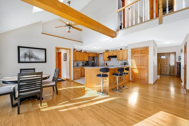 kitchen featuring a breakfast bar area, high vaulted ceiling, light wood-type flooring, stainless steel fridge, and beam ceiling