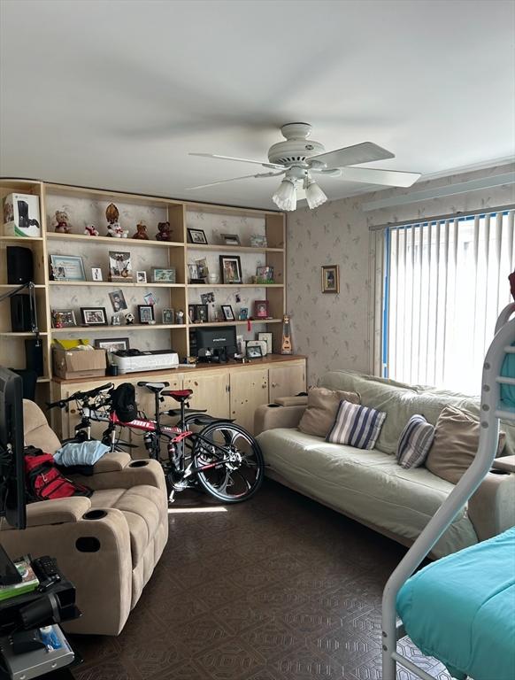 living area with a ceiling fan and wallpapered walls