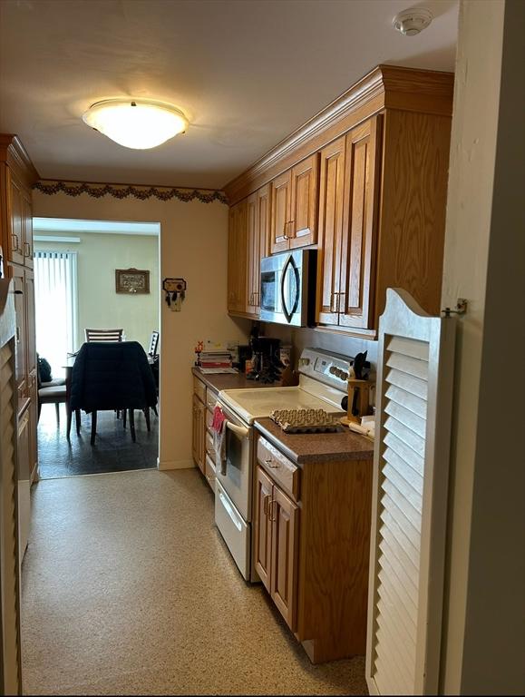 kitchen with dark countertops, stainless steel microwave, brown cabinetry, and white range with electric cooktop