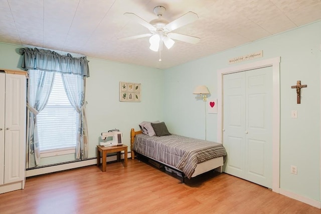 bedroom featuring light wood-style floors, a baseboard heating unit, and a ceiling fan