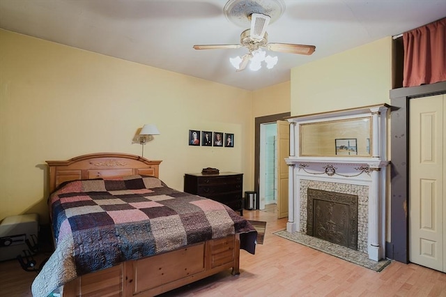 bedroom with light wood-style floors, a tiled fireplace, and ceiling fan