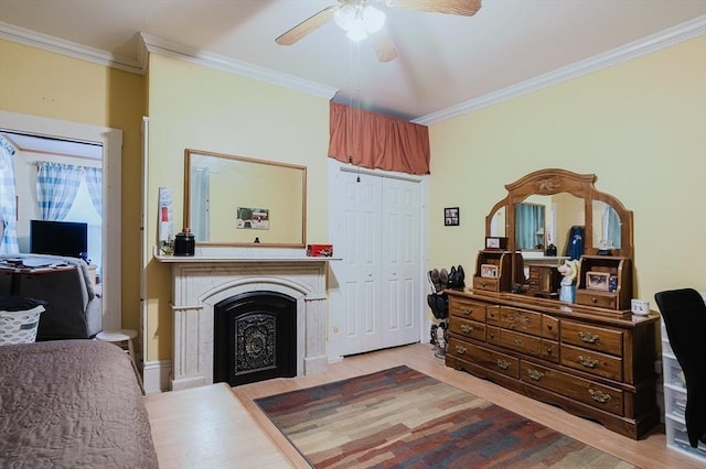 bedroom with ornamental molding, wood finished floors, a fireplace with flush hearth, a ceiling fan, and a closet