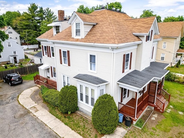 view of home's exterior with covered porch, a chimney, fence, and a shingled roof