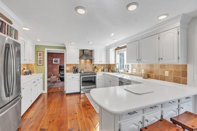 kitchen featuring crown molding, stainless steel appliances, white cabinets, kitchen peninsula, and wall chimney exhaust hood