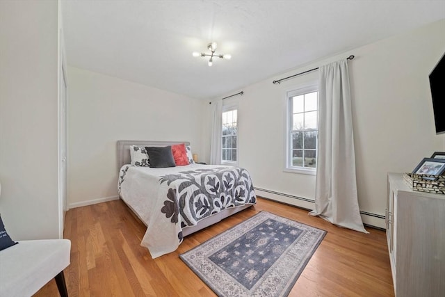 bedroom with baseboard heating, a notable chandelier, and light hardwood / wood-style floors