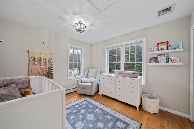 bedroom with a baseboard heating unit, a crib, and hardwood / wood-style flooring