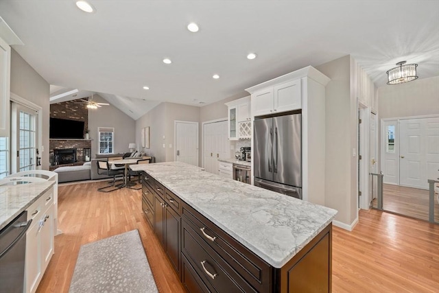 kitchen with a brick fireplace, a center island, appliances with stainless steel finishes, white cabinets, and ceiling fan with notable chandelier