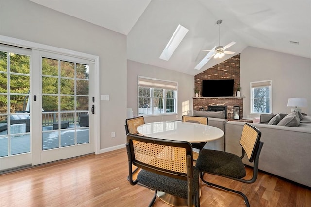 dining space with ceiling fan, a brick fireplace, lofted ceiling with skylight, and light hardwood / wood-style floors