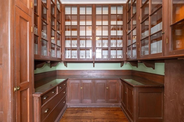 interior space featuring brown cabinetry, dark wood-style floors, dark countertops, and glass insert cabinets