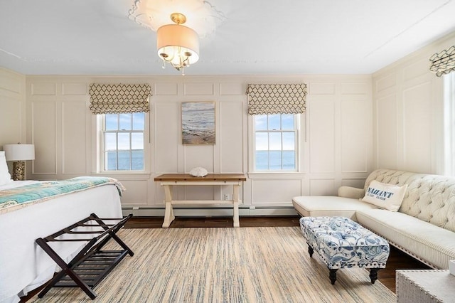 bedroom with wood finished floors, multiple windows, a baseboard radiator, and a decorative wall