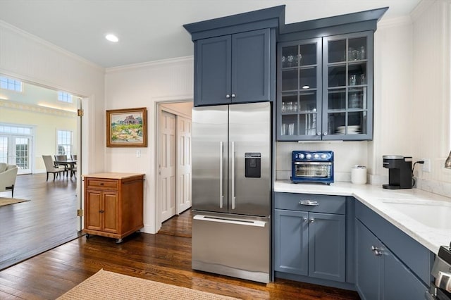 kitchen with stainless steel refrigerator with ice dispenser, dark wood finished floors, a sink, glass insert cabinets, and ornamental molding