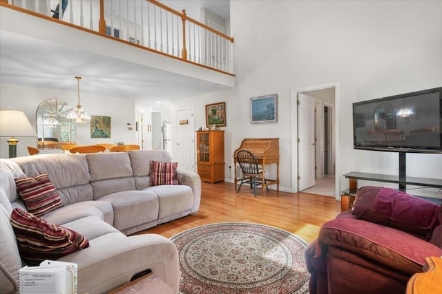 living room featuring an inviting chandelier, light wood-style floors, baseboards, and a high ceiling