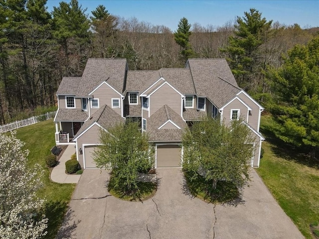 view of front of house with driveway, a wooded view, a shingled roof, a front yard, and fence