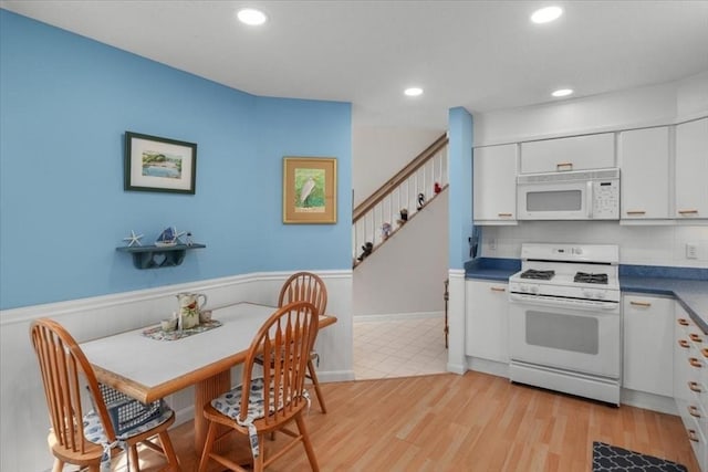 kitchen featuring light wood-style floors, white cabinets, wainscoting, and white appliances